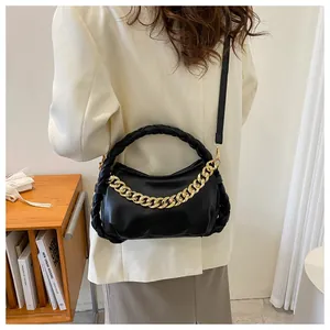 Detail of a black leather handbag featuring a chunky gold chain and a woven handle design
