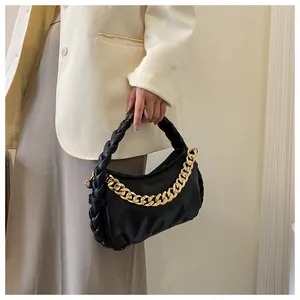 Close-up of black leather handbag with woven handle and chunky gold metal chain detail