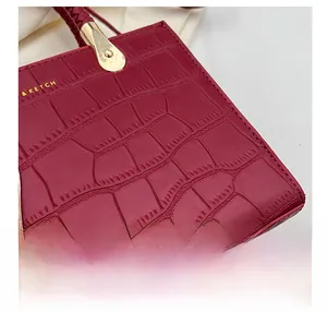Detail of burgundy crocodile embossed leather handbag with gold logo and woven handle