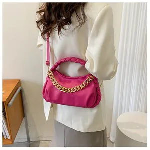 Detail of fuchsia leather bag with woven handle and gold chain on model in white suit