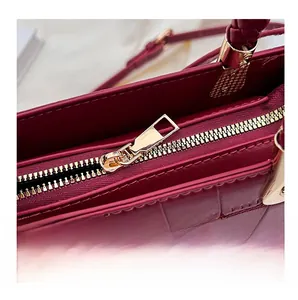 Macro shot of burgundy crocodile pattern handbag showing smooth golden zipper and woven handle