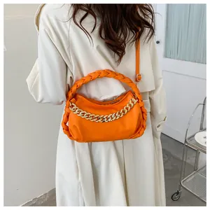 Detail of bright orange chain handbag with woven handle worn over a white coat