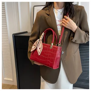 Detail of red crocodile texture handbag with woven handle and silk scarf accessory