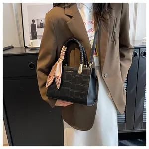 Detailed view of black crocodile pattern handbag with woven handle and silk scarf
