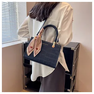 Detail of navy crocodile texture handbag with heart-patterned silk scarf and gold hardware