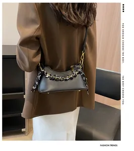 Detail of black crossbody bag with litchi texture and silk scarf chain handle on model