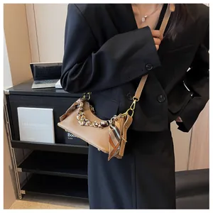 Brown lychee leather shoulder bag with gold chain and floral scarf on a modern desk