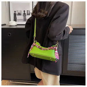 Close-up of bright green crescent crossbody bag with floral scarf chain and gold studs