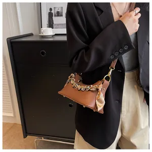 Brown leather handbag with scarf-wrapped handle and metal chain on a black cabinet