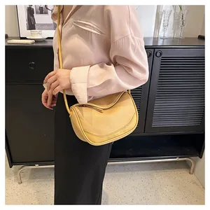 Close-up of beige lychee grain leather saddle bag on shoulder with sleek zipper detail