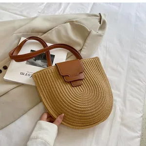 Detailed view of handmade woven straw bucket bag with dark brown leather straps and flap