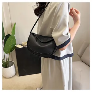 Detail of a black pebbled leather crossbody bag shown on a model for scale and fit