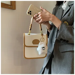 Dettaglio della borsa quadrata in pelle minimalista con profili a contrasto e ciondolo