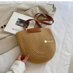Detail view of woven straw tote texture with brown leather flap and slim shoulder strap