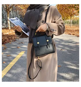 Detail of minimalist black leather crossbody bag featuring gold metal buckles and top handle
