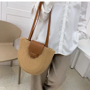 Detail of a half-round straw tote bag with layered brown leather flap and shoulder strap