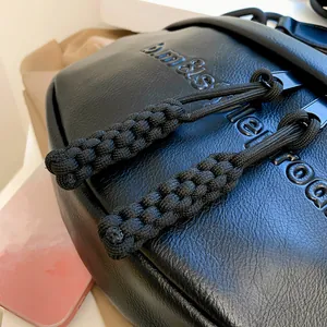 Close-up of black pleated moon bag with litchi grain leather and embossed logo detail
