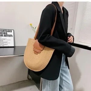 Detail of woven straw bucket bag featuring a brown leather flap and slender shoulder strap