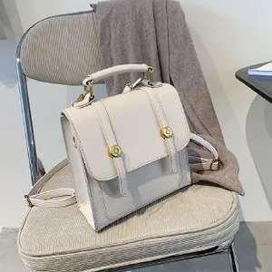 Minimalist cream leather backpack with gold buckle placed on a gray chair