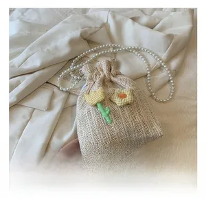 Détails du sac seau en paille avec patchs floraux et bandoulière perle sur blazer blanc