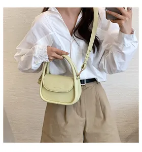 Detail of a pale yellow crossbody bag with T&M MODERN embossing and leather handle