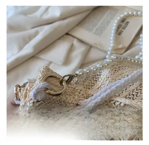 Détail du sac seau en paille avec ferrures dorées et bandoulière en perles élégante