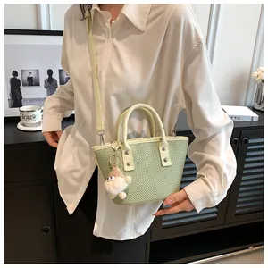 Detail of light green woven bucket bag with handles and cute plush charm pendant