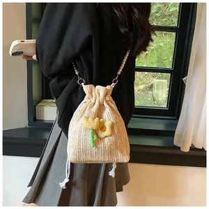Détail du sac seau en paille avec fleur 3D jaune et bandoulière en perles