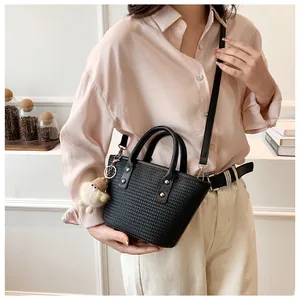Close-up of black woven leather bucket bag with cute plush bear charm on adjustable strap