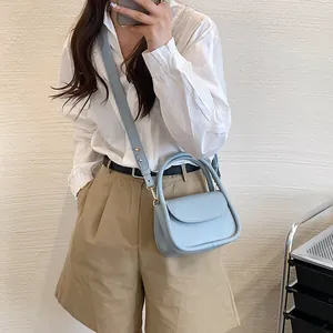 Minimalist light blue leather crossbody bag with rounded design and curved top handle