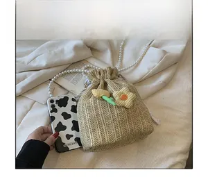 Détail du sac seau en paille tissée avec bandoulière perle et breloque à côté du téléphone