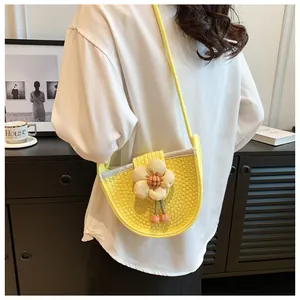Detail of a bright yellow woven crossbody bag with floral charms on a female model