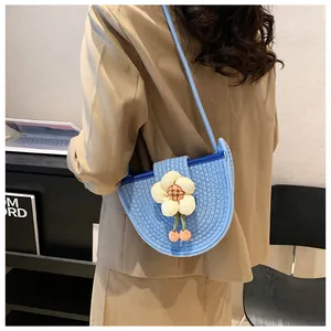 Detail of woven crossbody bag with white flower charm and pink pompom accents