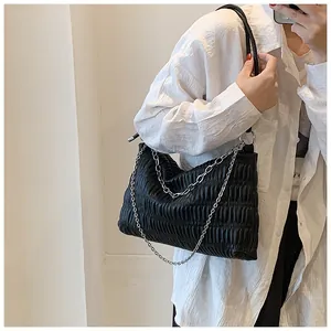Detail of black pleated tote bag with silver chain strap on a white shirt model
