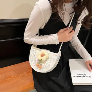 Fashionable woven half-moon crossbody bag with colorful patterns and floral charm