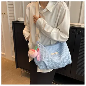 Detail of light blue ruched cloud bag with wide strap and peach plush pendant