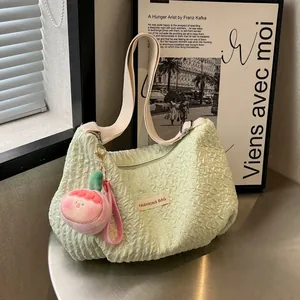 Light green ruched cloud bag with wide canvas strap and pink plush charm accessory