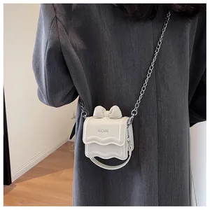 Detail van de witte mini crossbodytas met strikdecoratie en een zilveren ketting