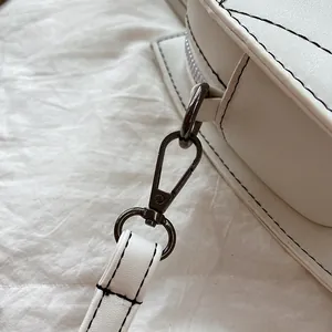 Detail van de donkere metalen haak en zwarte stiksels op de witte lederen tas