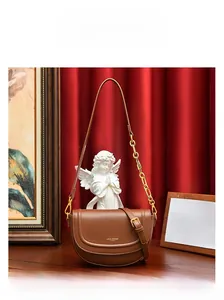 Détail d'un sac besace en cuir marron avec chaîne dorée et logo de la marque