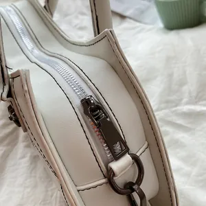 Gedetailleerde close-up van de donkergrijze metalen rits op de witte lederen tas