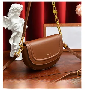 Détail d'un sac besace en cuir marron avec chaîne dorée et logo sur fond de velours