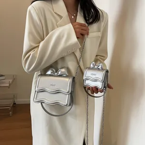 Mini zilveren metallic handtas met strikontwerp en kettingband gedragen door model