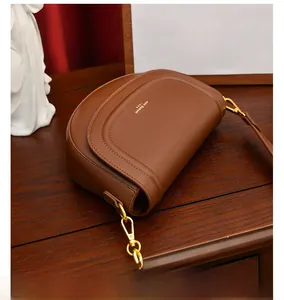 Gros plan d'un sac besace en cuir marron avec boucle dorée et logo sur surface en bois