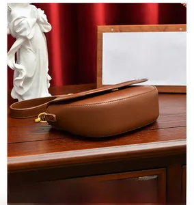 Vue de dessus d'un sac besace marron en cuir sur velours rouge avec boucles dorées