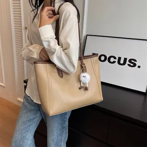Detail view of large beige PU tote bag with brown straps and plush charm on model