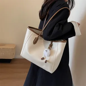 Detail of a large white PU tote bag with brown straps and a cute plush ball charm