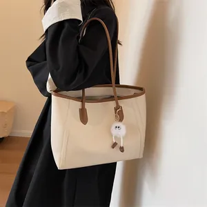 Detailed side view of a large beige tote bag with brown straps and a cute plush charm