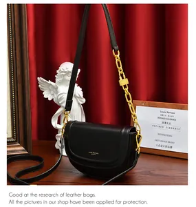 Détail du sac selle en cuir noir avec bandoulière chaîne dorée et logo embossé chic