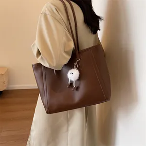 Detail of deep brown PU leather tote bag with creative plush charm on a model